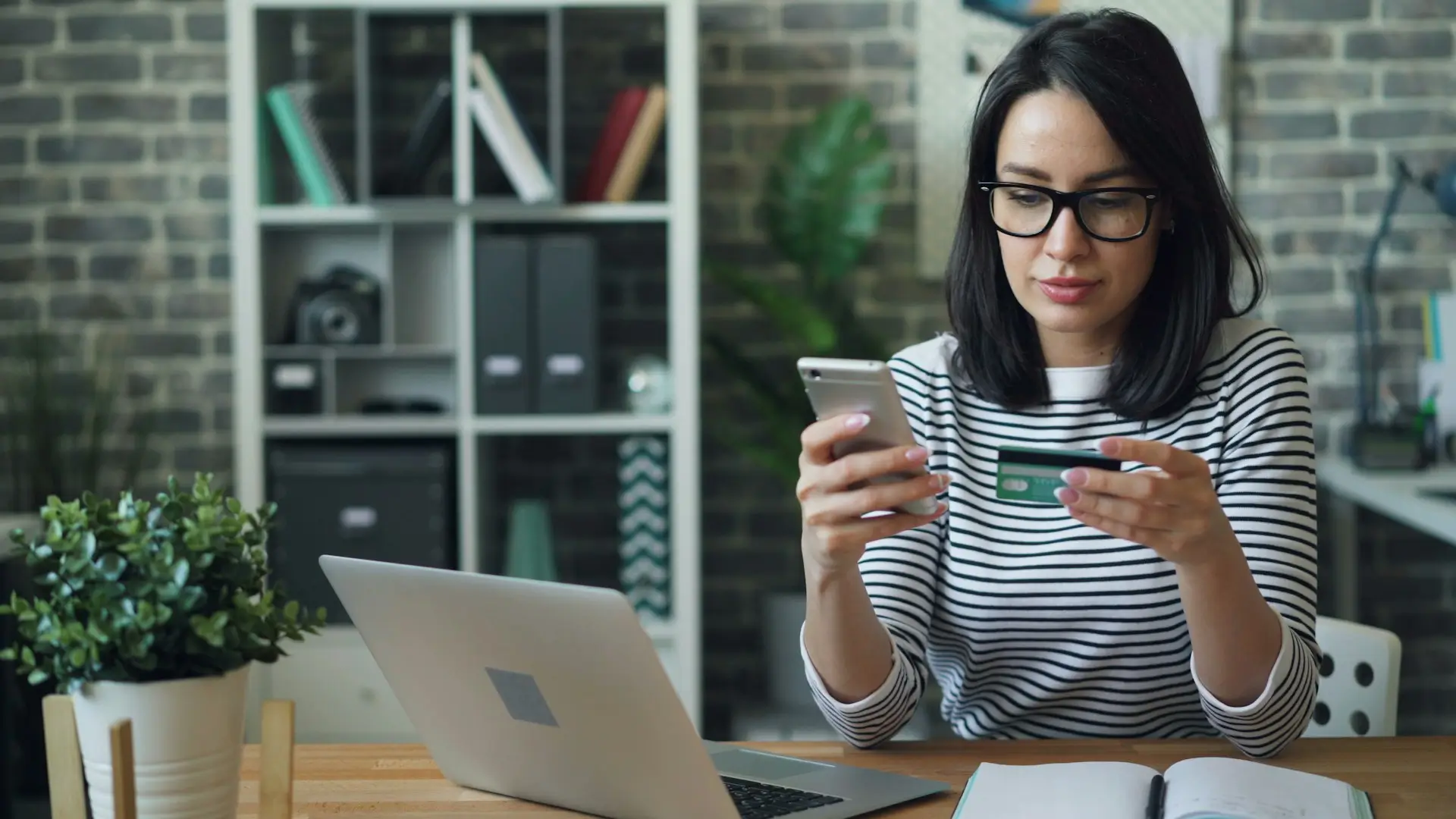 Portrait of young woman making payment with credit card using smartphone at work