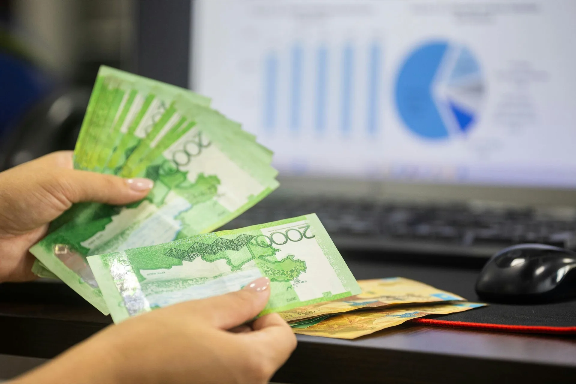 Counting cash with financial data on screen (Bia Limova, Pexels)