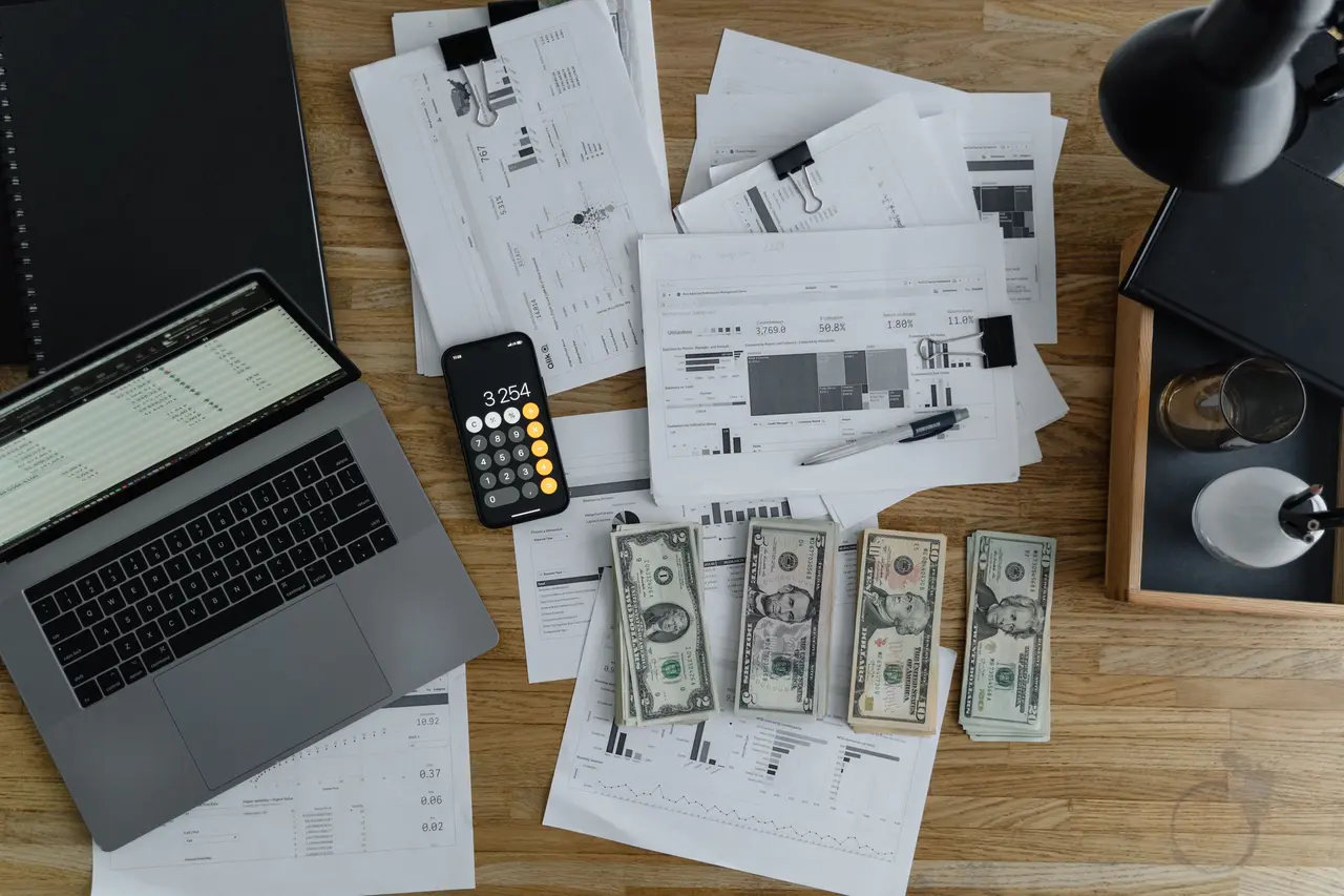 A laptop near dollars and papers on a wooden table