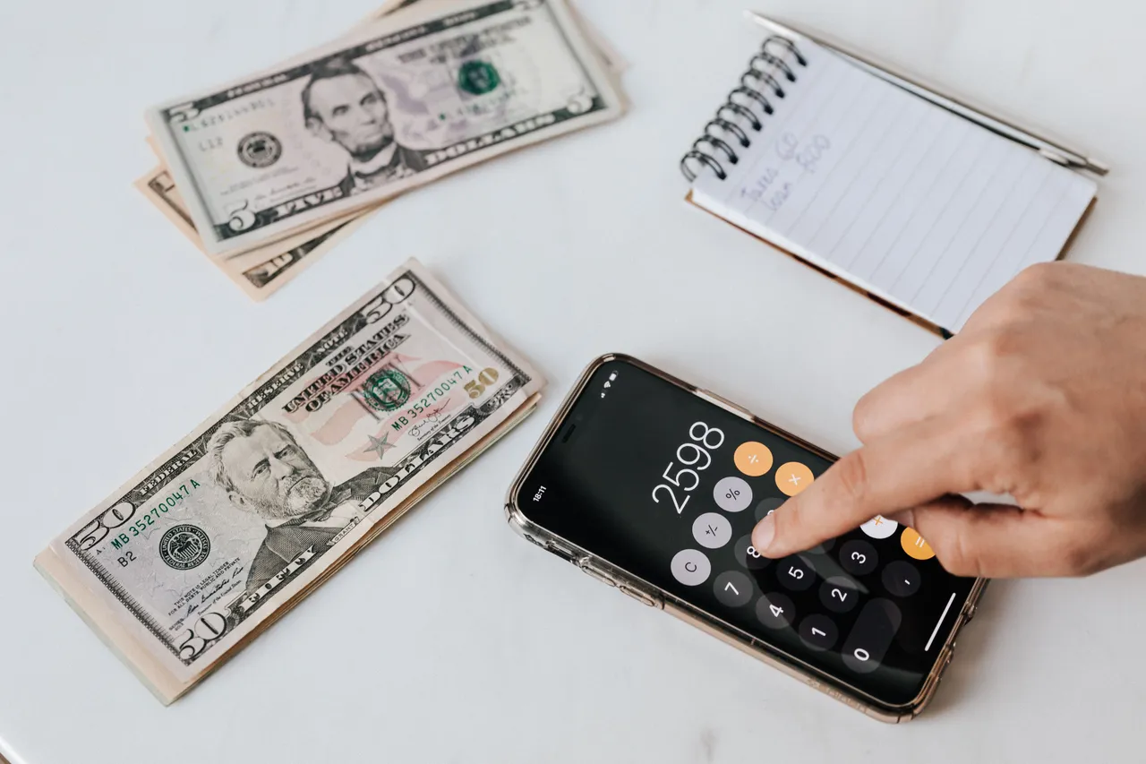 Financier using calculator on smartphone near dollar banknotes