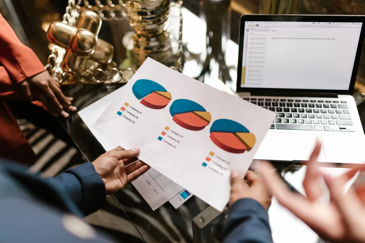A person holding a pie chart report next to a laptop