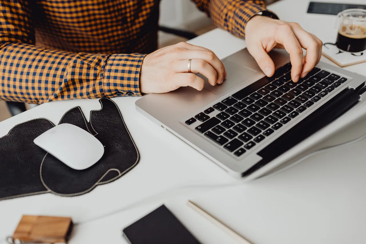 Person typing on a laptop surrounded by documents and a cup of coffee